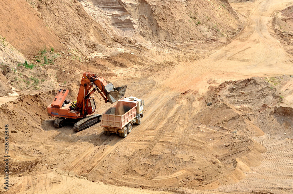 Excavator developing the sand on the opencast and loading it to the heavy dump truck. Processing of loose material in mining quarry. Drill, breaking, processing plant, crushing and screening Excavator developing the sand on the opencast and loading it to the heavy dump truck. Processing of loose material in mining quarry. Drill, breaking, processing plant, crushing and screening