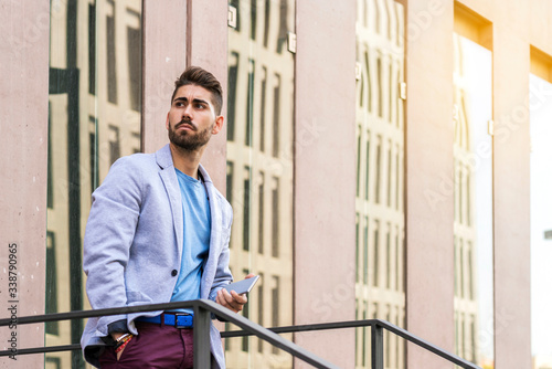 Portrait of a happy bearded young man holding a mobile phone while standing outdoors and looking away