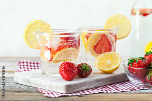 Refreshing homemade lemonade with fresh strawberry, lemon and ice. Healthy cold drink, low calories. Tasty cool summer beverage. Wooden white background, two glasses. Copy space for text