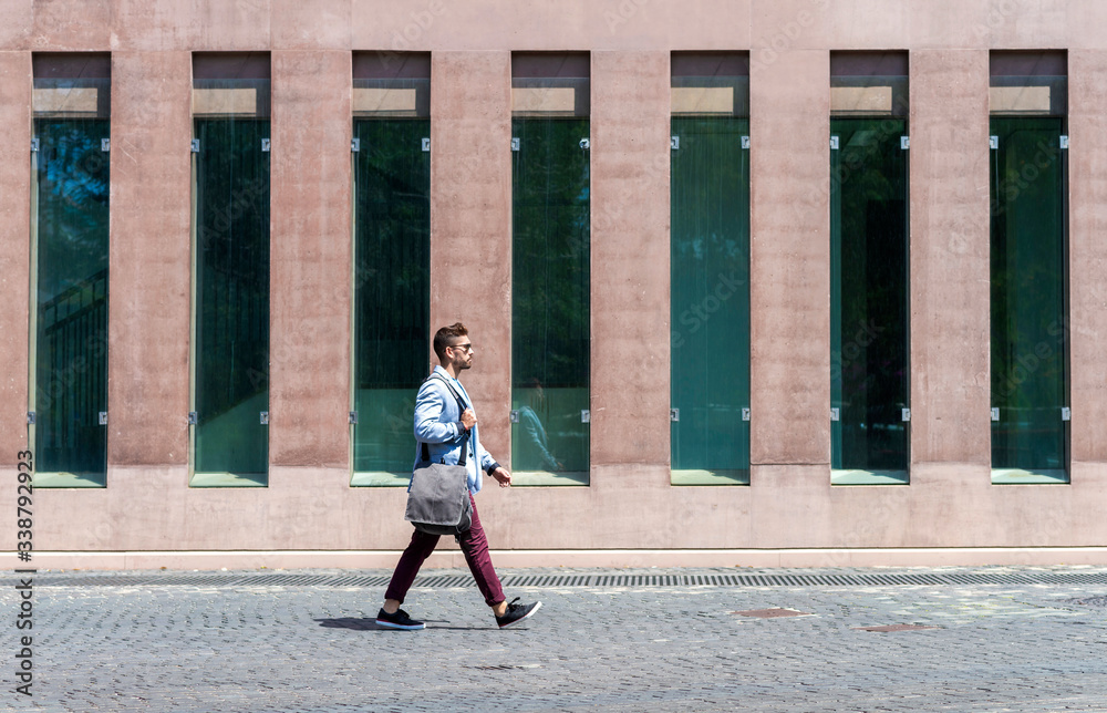 Portrait of a trendy young man walking while holding a shoulder bag