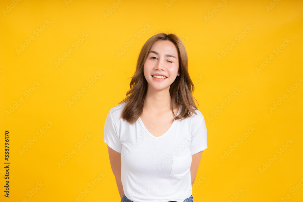 Portrait happy young asian woman laughing blink, wink eye joyful funny positive emotion in white t-shirt, Yellow background isolated studio shot and copy space. Portrait happy young asian woman laughing blink, wink eye joyful funny positive emotion in white t-shirt, Yellow background isolated studio shot and copy space.