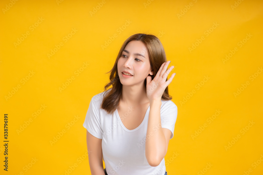 Portrait happy young asian woman smiling hand holding ear listening something positive emotion in white t-shirt, Yellow background isolated studio shot and copy space, gossip secret concept. Portrait happy young asian woman smiling hand holding ear listening something positive emotion in white t-shirt, Yellow background isolated studio shot and copy space, gossip secret concept.