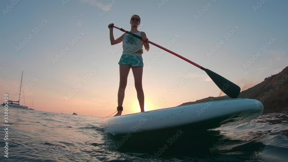 Young woman paddle the SUP board in the sea at sunset