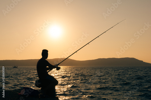 Silhouette of a young boy holding a rod and fishing at sunset