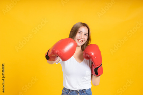 Portrait happy young asian woman with boxing glove punching hit or self defend in white t-shirt, Yellow background isolated studio shot and copy space. © Kiattisak