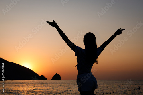 Silhouette of a girl at sunrise/sunset on the background of the sea and mountains