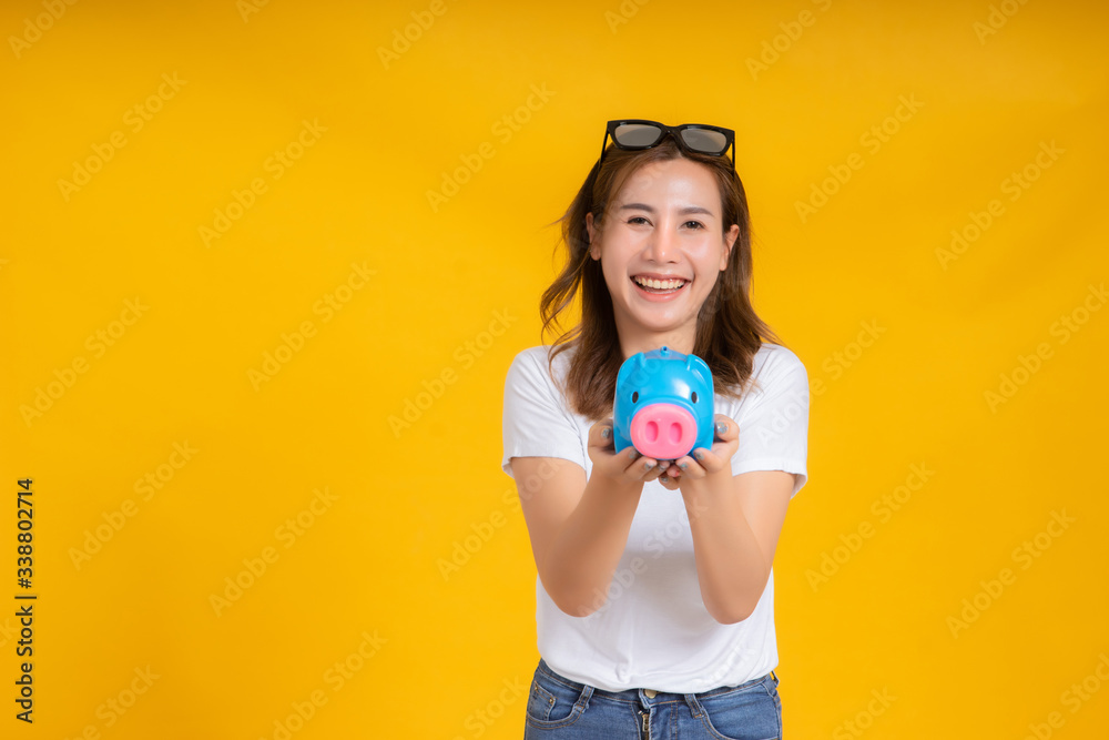 Portrait happy young asian woman holding piggybank saving money for future and business earning income positive emotion in white t-shirt, Yellow background isolated studio shot and copy space. Portrait happy young asian woman holding piggybank saving money for future and business earning income positive emotion in white t-shirt, Yellow background isolated studio shot and copy space.