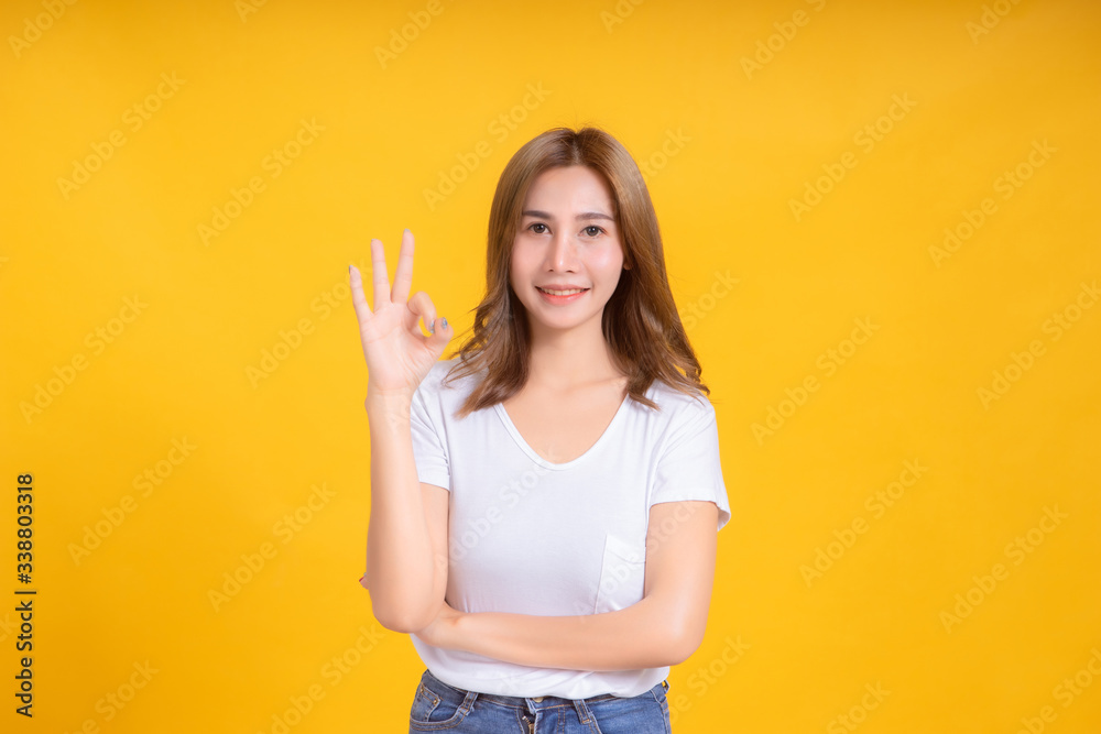 Portrait young happy asian woman ok gesture hand symbol for advertising promotion sale discount in white t-shirt, Yellow background isolated studio shot and copy space.