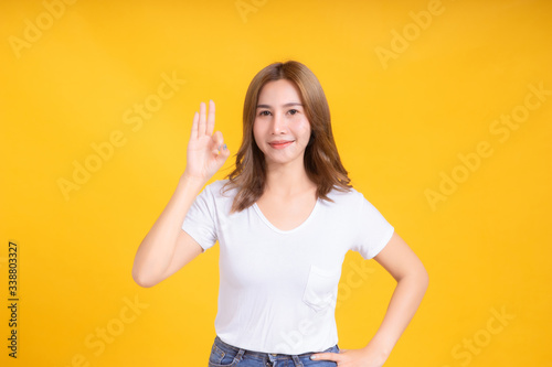 Portrait young happy asian woman ok gesture hand symbol for advertising promotion sale discount in white t-shirt, Yellow background isolated studio shot and copy space. © Kiattisak