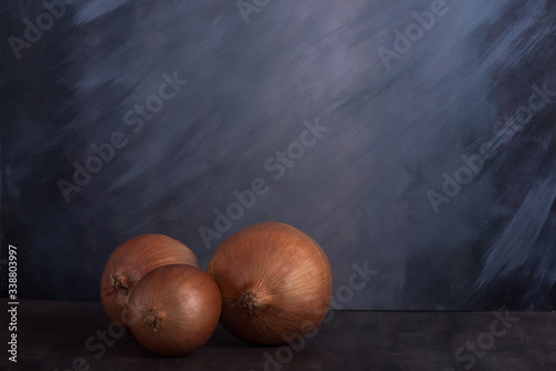 Onions in the peel on a dark vintage background. Artistic depiction of vegetables on a dark textural background
