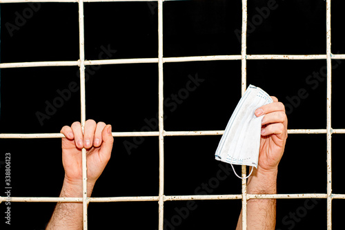 concept of restriction during the pandemic and quarantine of a person s hand behind an iron bars in his hand medical hygiene mask photo