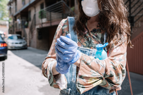 Young and elegant girl with protective gloves and flu mask disinfects her hands with gel . Concept of health and prevention. © JAVIER LARRAONDO