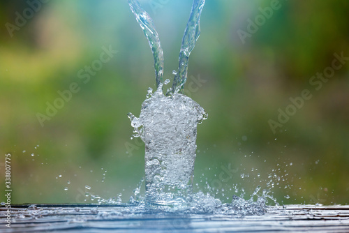 Drink water pouring in to glass over sunlight and natural green background.Select focus blurred background.Fersh Clean water splash.