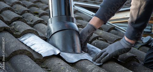 The plumber. Placing a exhaust air duct at rooftop. Arranging the lead on the rooftiles. photo