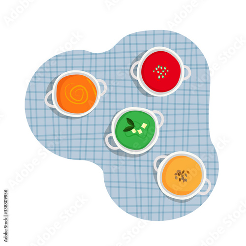 Healthy cuisine set of white ceramic pots of various cream soups - tomato, carrot, broccoli, pumpkin cream soup on blue tartan table cloth background. 