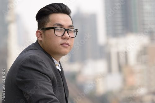 Young overweight Asian businessman with eyeglasses thinking in the city