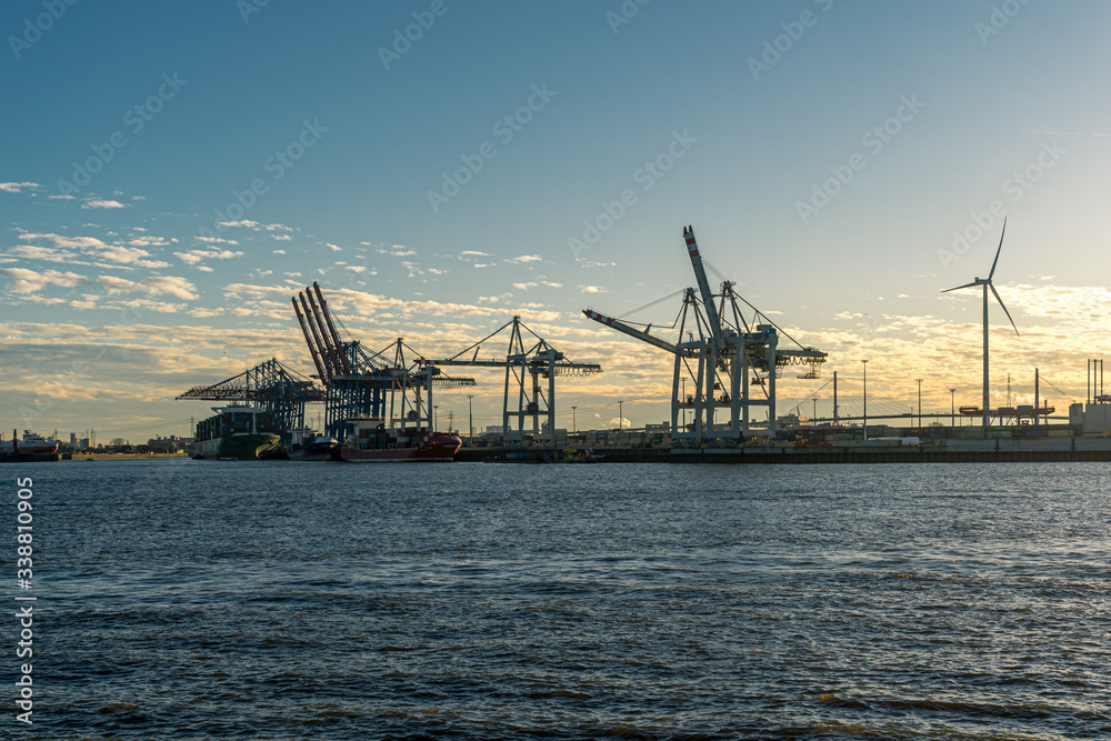 Hamburg container port with some ships loading and cranes transporting container to the freighters at sunset/twilight