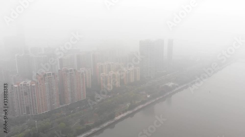 Guangzhou city immersed in morning fog, aerial shot. Green linear park at Pearl River embankment, modern residential quarters at Tianhe District dissolve in mist at distance. photo
