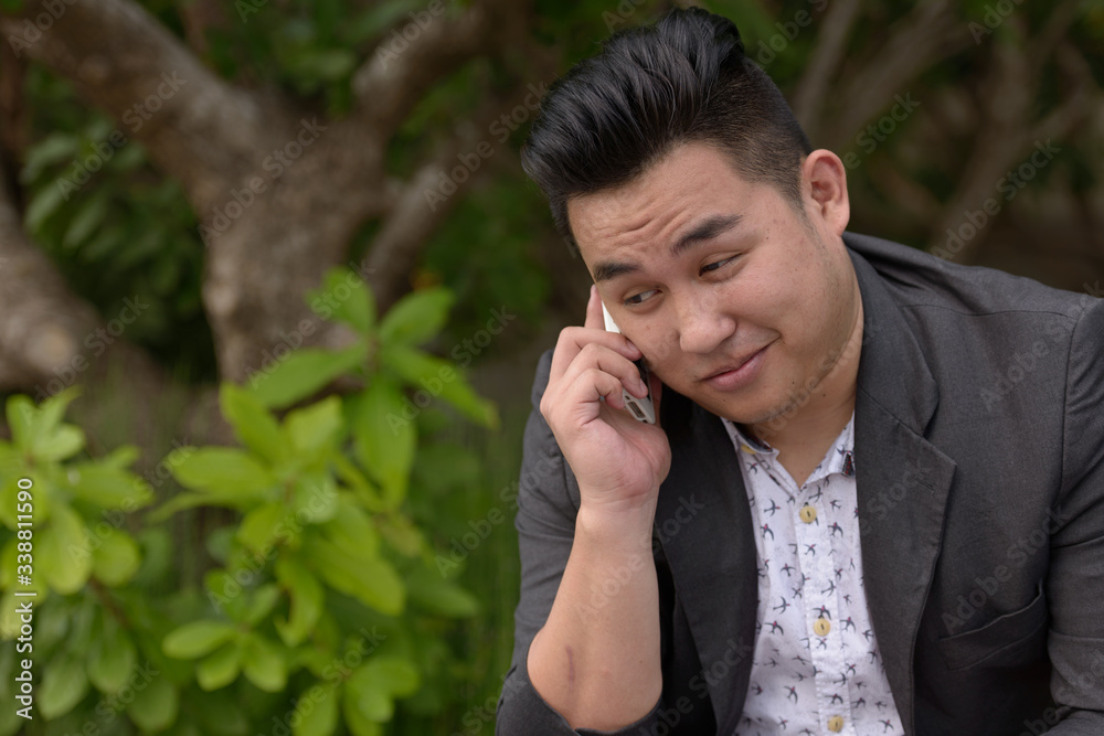 Young overweight Asian businessman talking on the phone at the park Young overweight Asian businessman talking on the phone at the park