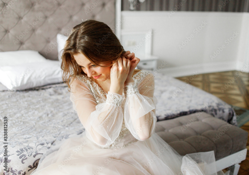 Sweet bride in a natural way puts an earring on her ear. Sunlight shines from the window. Bride morning. Sweet bride in a natural way puts an earring on her ear. Sunlight shines from the window. Bride morning.