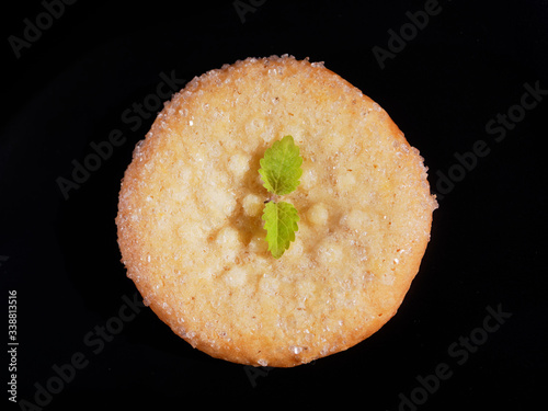 Appetizing sugar cookies on a black background. One cookie with lemon balm, top view.