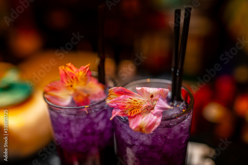 A refreshing violet alcoholic drink in the big cocktail glass decorated with a red flower on the bar counter. Close-up