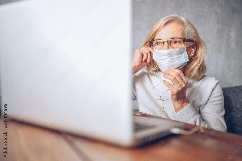 Technology, old age and people concept - lonely sad older senior woman in face medical mask working and making a video call with laptop computer at home during coronavirus COVID19 pandemic. Stay home Technology, old age and people concept - lonely sad older senior woman in face medical mask working and making a video call with laptop computer at home during coronavirus COVID19 pandemic. Stay home