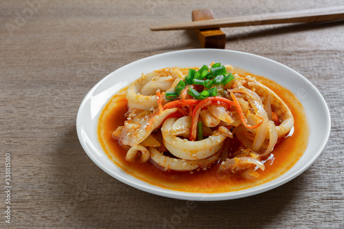 close up of stir fried squid with kimchi in a ceramic dish on wooden table. homemade style food concept.