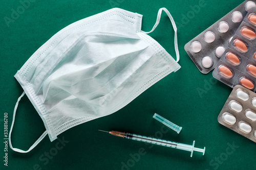 Medical mask, syringe and pills on green background. Corona virus or covid 19 disease treatment or vaccine research concept