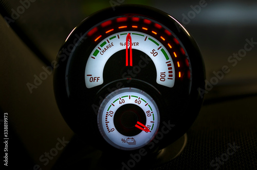Close up of illuminated power meter displays state of charge and current level of power delivery, energy regeneration. Circular car counter in full electric vehicle at night.