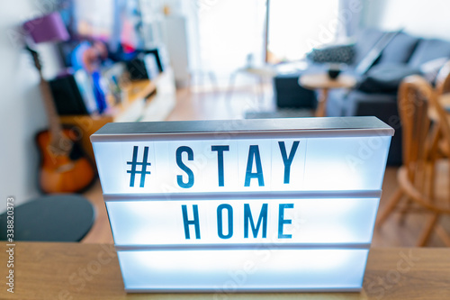 Coronavirus home sign lightbox with text hashtag #STAYHOME glowing in light. COVID-19 banner to promote self isolation staying at home. Apartment background