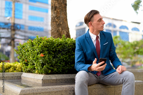 Mature handsome Italian businessman relaxing outside of the building