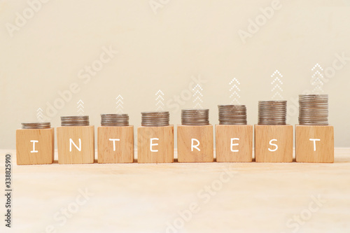 Interest on wooden cube and coins stacked in bar graph with upward arrow on top.