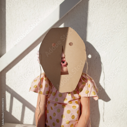 Portrait of a girl. A child hides his face behind a cardboard mask, indoor photo