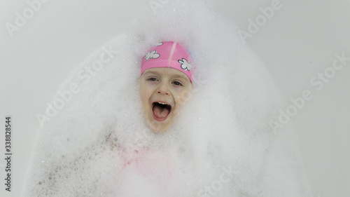 Cute blonde girl takes a bath in swimwear. Little child lying in the bath
