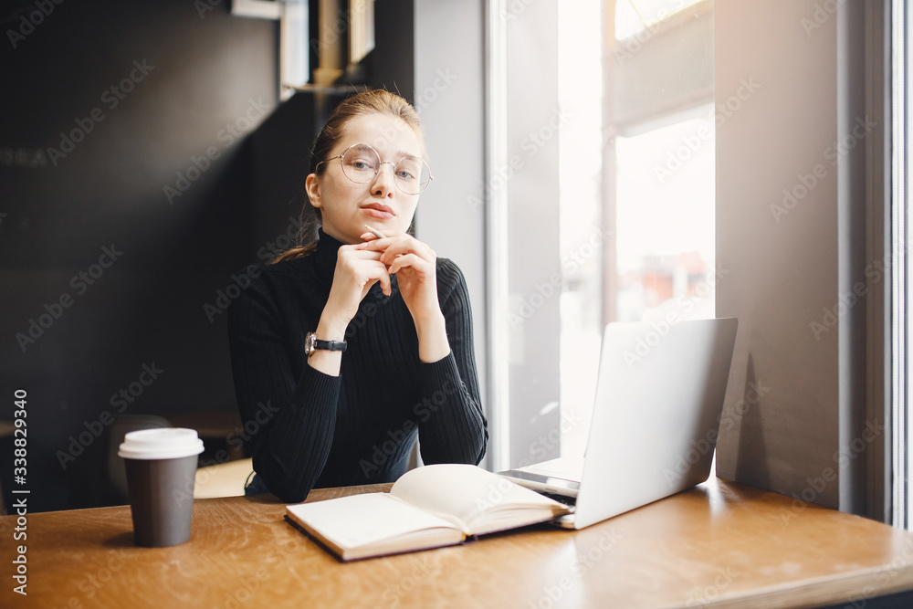 Young woman freelancer is working with laptop and black note in dark cafe. Concept customer search and problem solving startup. Young woman freelancer is working with laptop and black note in dark cafe. Concept customer search and problem solving startup.