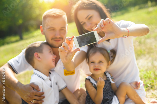 Happy family making selfie on smartphone. Happy people resting together with their children outdoors.