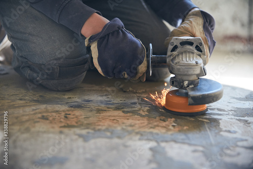 A man in gloves and protective knee pads on the legs grinds the floor with a grinder photo