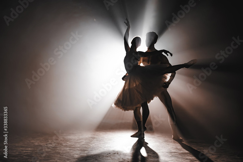 Foto Graceful ballerina and her male partner dancing elements of classical or modern ballet in dark with floodlight backlight