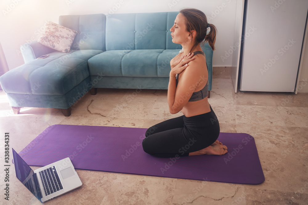 Lessons of meditation breathing and yoga at home, a woman is engaged in the living room in front of a laptop - obrazy, fototapety, plakaty 