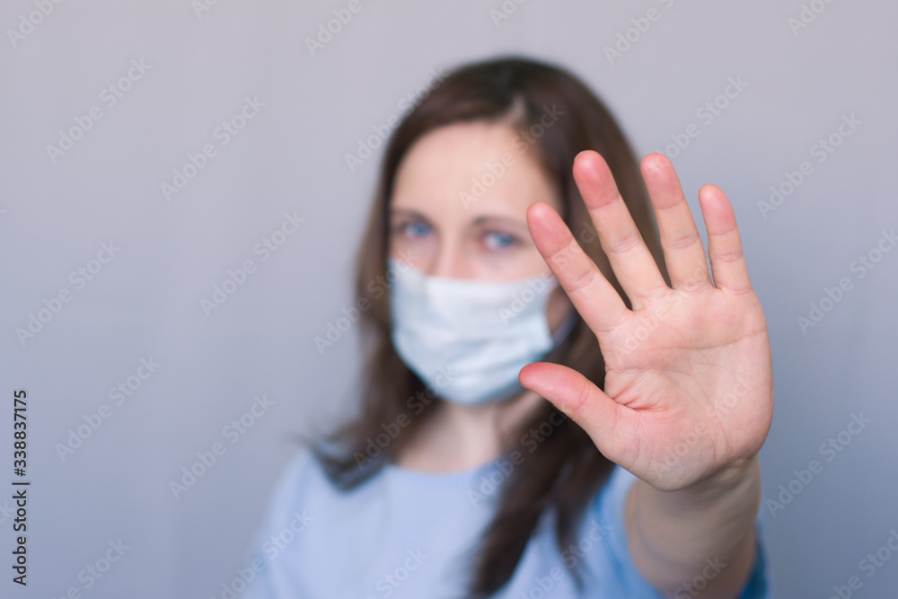 Woman in a medical protective mask shows a stop sign. Woman in a medical protective mask shows a stop sign.
