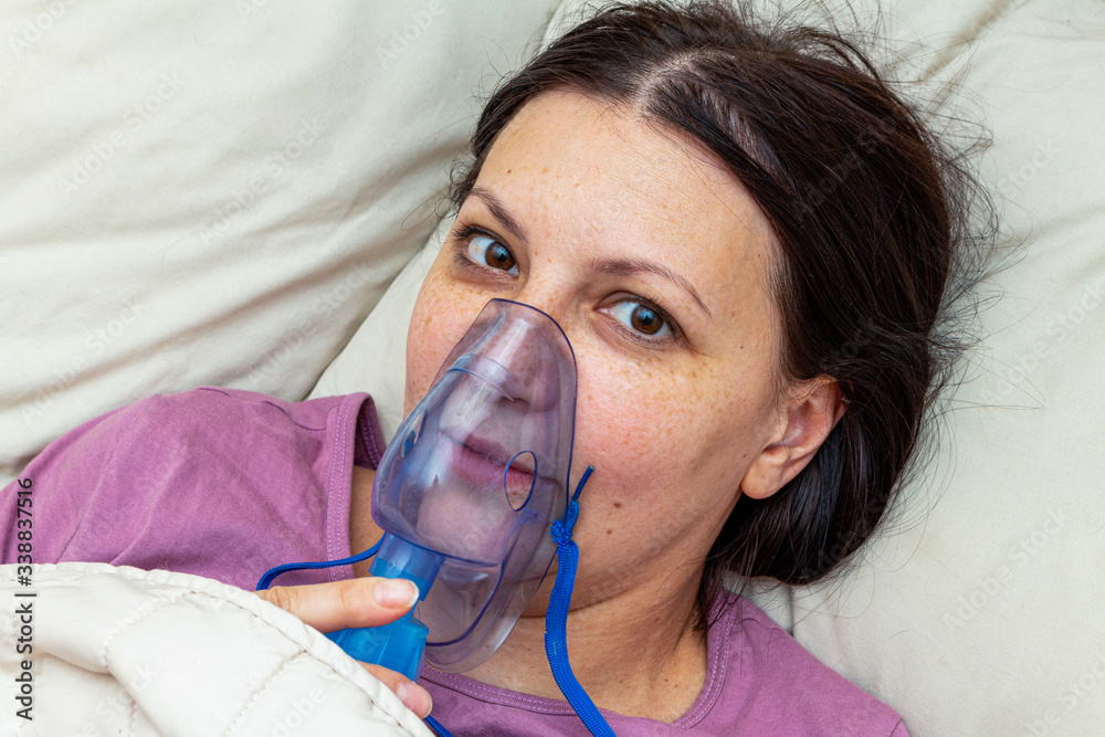 sick woman suffers with viral flu in bed in a inhalation mask