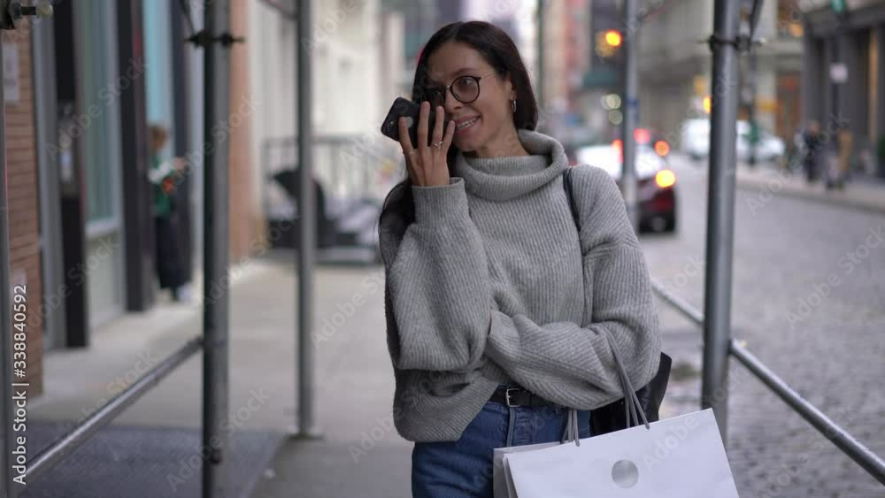 Happy hipster girl in trendy outfit walking in city downtown and recording voice message via mobile dictaphone connected to 4g wireless in roaming for sending mail, cheerful female with smartphone 

