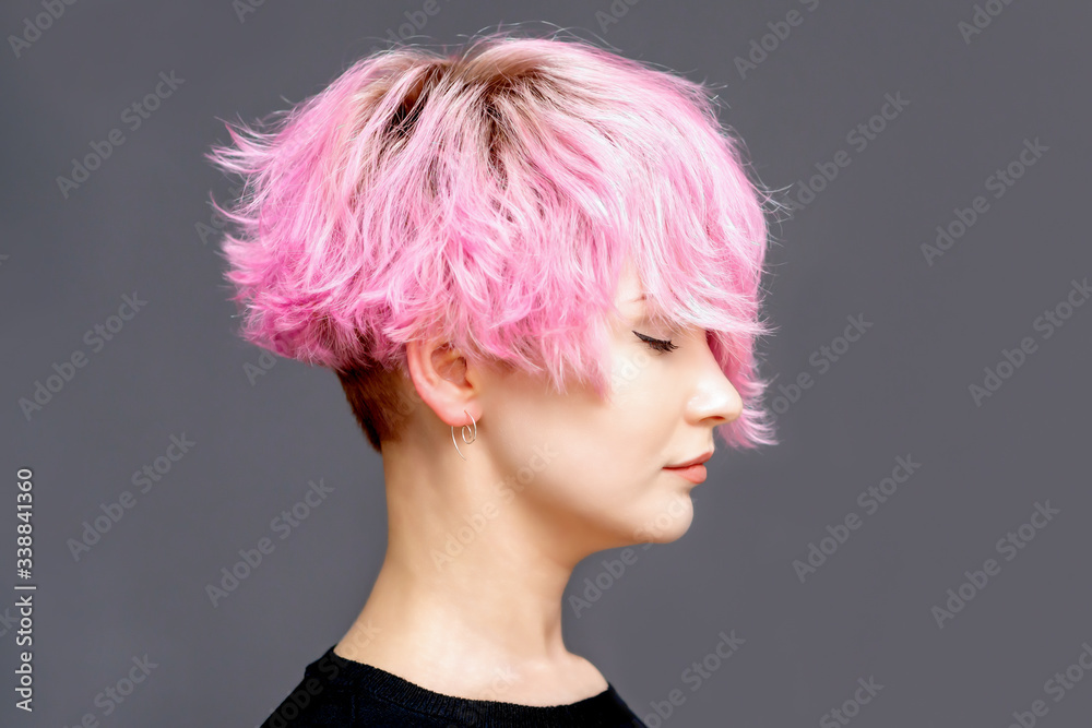 Woman with pink hairstyle stands with closed eyes side view on gray background with copy space.