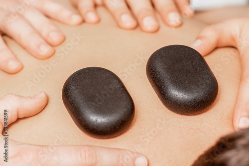 Hands of massage therapists doing back massage while hot stones on back of man close up in spa.