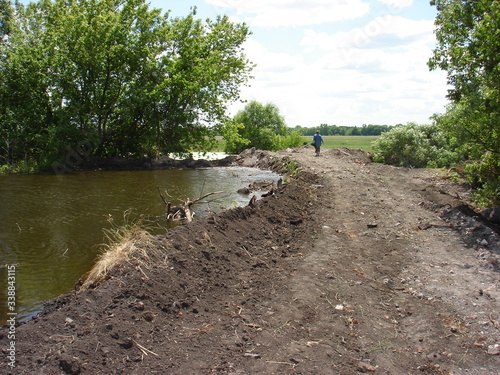 Fotografie The river is blocked by an earthen embankment dam on a summer day