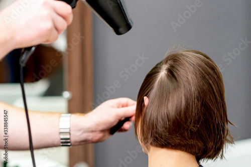 Close up of professional hairdresser is drying hair of woman, back view in hair salon.