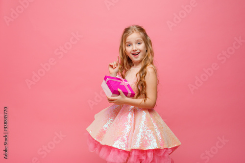 a little girl holding a gift in her hands smiles on a pink background. © Olesya Pogosskaya