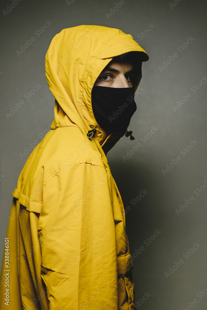 young skinny man wearing a yellow hooded jacket and black face mask with an aggressive serious look young skinny man wearing a yellow hooded jacket and black face mask with an aggressive serious look