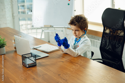 Caucasian teenboy as a doctor consulting for patient, giving recommendation, treating. Little doctor during funny wearing protective gloves. Concept of childhood, human emotions, health, medicine. photo